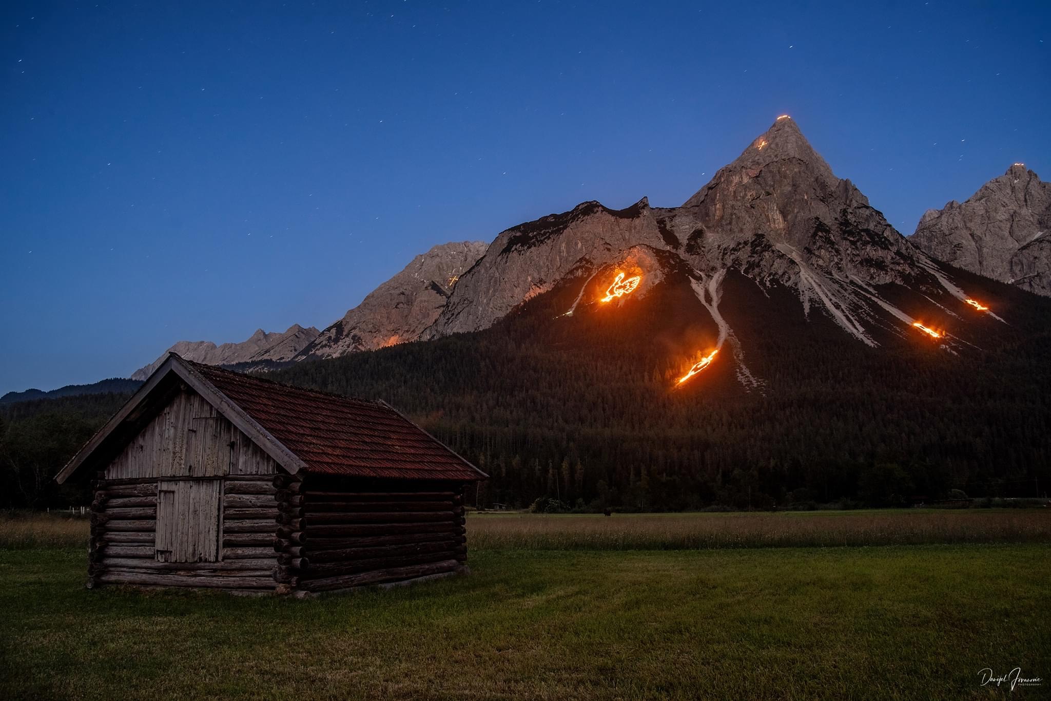 Ein Bergpanorama mit Sommersonnwendfeuer, die als Tiere gestaltet sind.